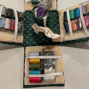 May include: A green fabric sewing box with multiple compartments filled with spools of thread in various colors. The box is open and the compartments are visible. The thread is wrapped in clear plastic.