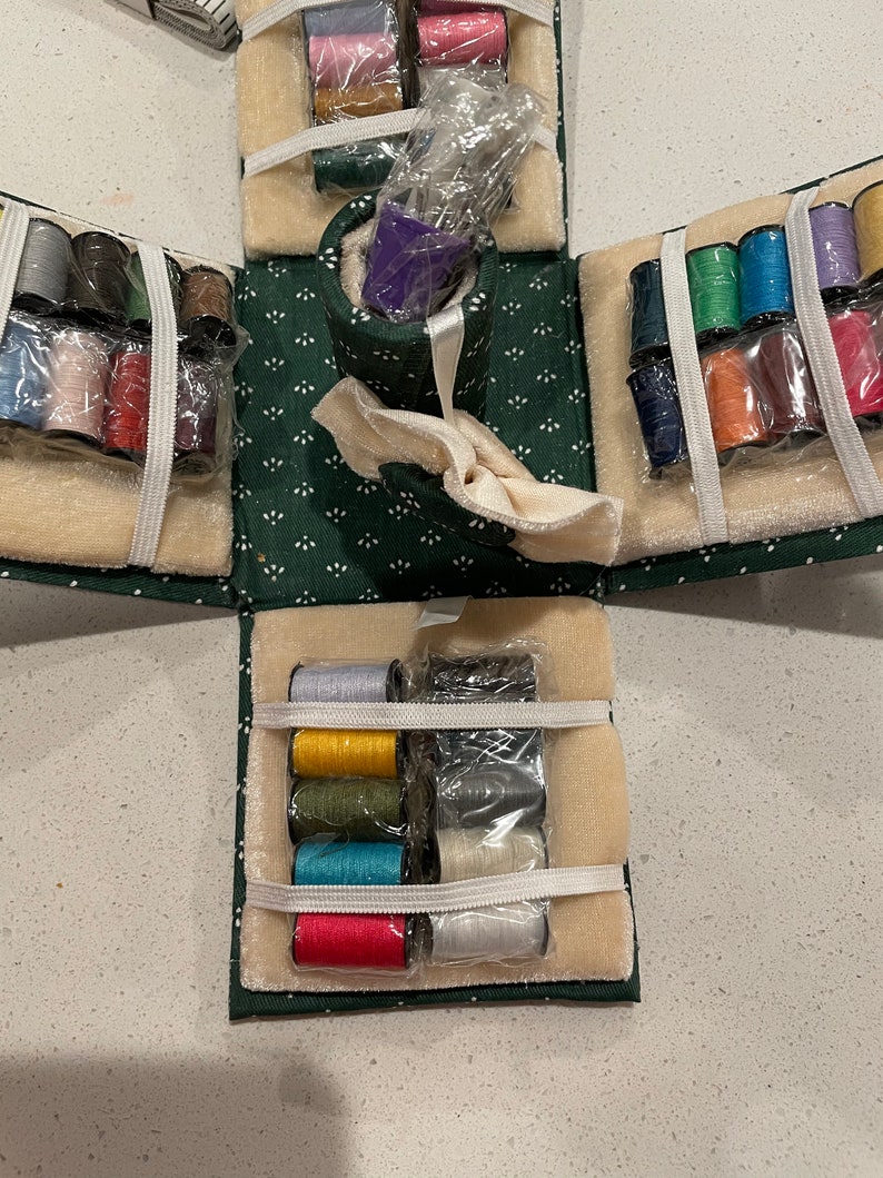 May include: A green fabric sewing box with multiple compartments filled with spools of thread in various colors. The box is open and the compartments are visible. The thread is wrapped in clear plastic.