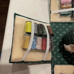 May include: A green velvet sewing box with a beige velvet interior. The box contains a variety of spools of thread in different colors, including yellow, gray, black, green, red, and pink.
