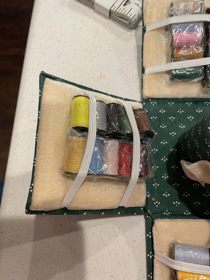 May include: A green velvet sewing box with a beige velvet interior. The box contains a variety of spools of thread in different colors, including yellow, gray, black, green, red, and pink.