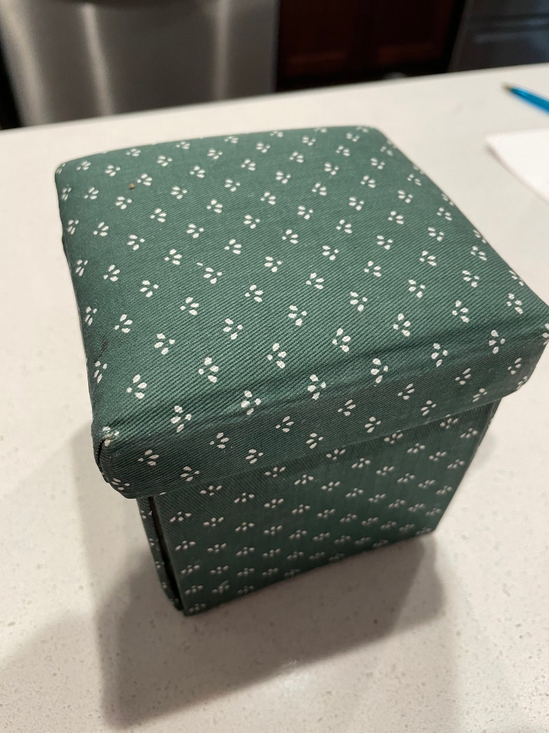 May include: A green fabric storage box with a white floral pattern. The box is square and has a hinged lid.