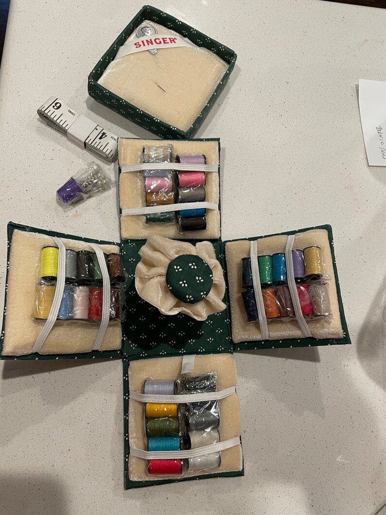 May include: A green Singer sewing kit with a variety of colored threads, needles, and a pincushion. The kit is open and the different compartments are visible.
