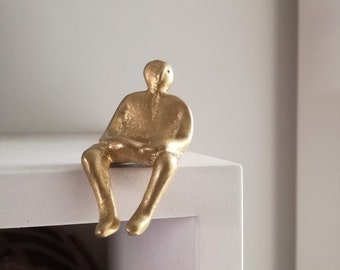 Seated man figure, brass sculpture of sitting man, little figure sculpture perched on the edge of a shelf, oxidised brass, tiny figurine