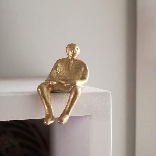 Seated man figure, brass sculpture of sitting man, little figure sculpture perched on the edge of a shelf, oxidised brass, tiny figurine