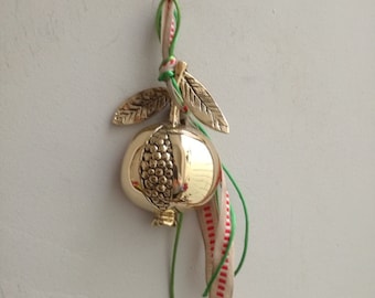 Gold pomegranate sculpture with seeds, tied with beige, green ribbons, solid brass pomegranate on leafy  twig, half pomegranate sculpture