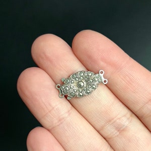 Puede incluir: Cierre de tono plateado con un diseño floral engastado con piedras de marcasita.