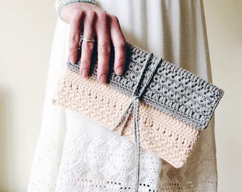 May include: A crocheted clutch purse in two shades of pink and gray. The purse is tied with a gray ribbon.