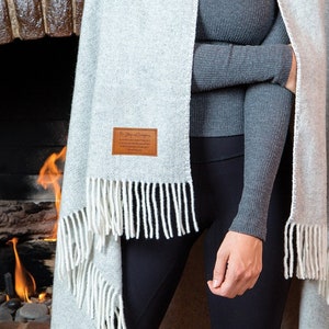 May include: A gray and white fringed scarf with a brown leather tag that reads "The Story of Company".