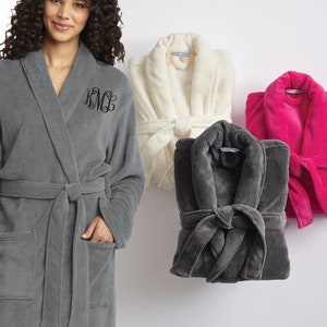 May include: Three plush robes in gray, white, and pink. The gray robe has a black embroidered monogram on the left chest. The robes have a shawl collar and a tie belt.