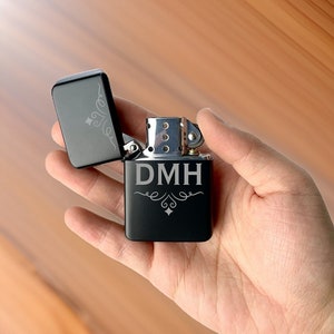May include: Black lighter with a silver hinge and a personalized inscription that reads "DMH" with decorative flourishes.