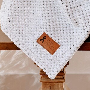 May include: White waffle knit throw blanket with a brown leather tag that says "Made with Love". The blanket is draped over a wicker basket.