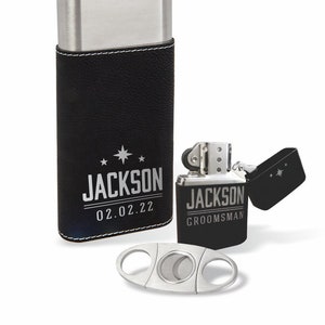 May include: A black leather cigar case with a silver metal top and a silver metal cigar cutter. The case has the name "JACKSON" and the date "02.02.22" engraved on it. A silver metal lighter with the name "JACKSON GROOMSMAN" engraved on it is also included.