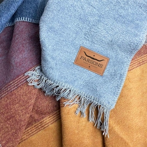 May include: A blue, brown, and gold striped throw blanket with a leather tag that says "Parsons Ranch & Ranch".