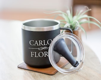 May include: A black stainless steel travel mug with a clear lid and a black silicone straw. The mug has the name "CARLO FLOR" engraved on the side.