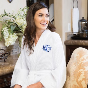 May include: White waffle-weave robe with a blue monogram. The robe has a shawl collar and a matching belt. The monogram is in a script font. The robe is made of a soft, absorbent material.