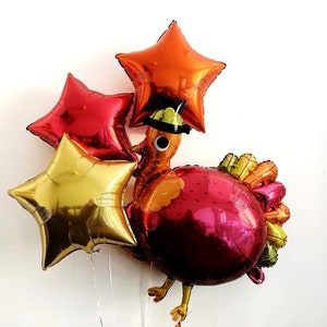 May include: Thanksgiving-themed balloon arrangement featuring a turkey and star-shaped balloons. The turkey balloon is primarily red with orange and yellow accents, wearing a pilgrim hat. Three star balloons in gold, red, and orange complete the festive display.