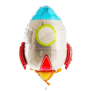 K&ouml;nnte beinhalten: Ein silberner Folienballon in Form einer Rakete mit roten Flossen, einem blauen Oberteil mit wei&szlig;en Punkten und einem gr&uuml;n-wei&szlig;en Bullauge. Der Raketen-Auspuff ist gelb und orange.