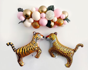 May include: A pink, gold, and white balloon garland with a tiger and leopard balloon. The balloons are arranged in a cluster and have a jungle theme.