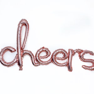 Könnte beinhalten: Rosen goldene Folien-Buchstabenballons, die das Wort "cheers" buchstabieren.