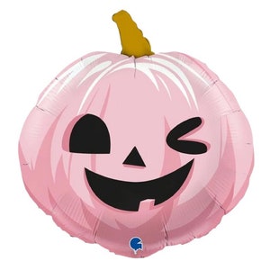 May include: A pink pumpkin balloon with a winking face. The balloon is made of foil and has a shiny finish.