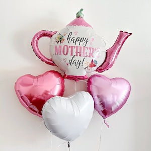 Può includere: Un palloncino a forma di teiera rosa e bianco con il testo "happy Mother's day!" circondato da tre palloncini a forma di cuore rosa.