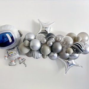 May include: A silver astronaut-shaped balloon and a cluster of gray, silver, and marble-patterned balloons. The balloon arrangement includes star-printed balloons and star-shaped foil balloons, creating a space-themed decoration.