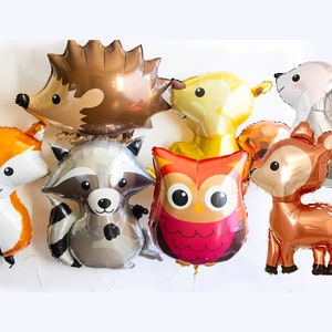 May include: A set of eight foil balloons featuring various woodland animals, including a fox, raccoon, owl, deer, hedgehog, bunny, and two bears. The balloons are all in different colors and have a shiny finish.