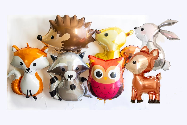 May include: A set of eight foil balloons featuring various woodland animals, including a fox, raccoon, owl, deer, hedgehog, bunny, and two bears. The balloons are all in different colors and have a shiny finish.