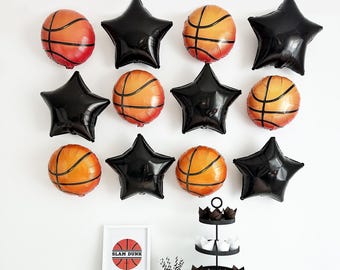 Puede incluir: Un conjunto de decoración para fiestas con temática de baloncesto. Incluye globos con forma de balón de baloncesto y estrella de color naranja y negro, una impresión enmarcada de "Slam Dunk", un soporte para cupcakes de varios niveles y cupcakes.