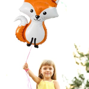 May include: A young girl in a yellow dress holds a large orange and white fox-shaped balloon with pink ribbon.