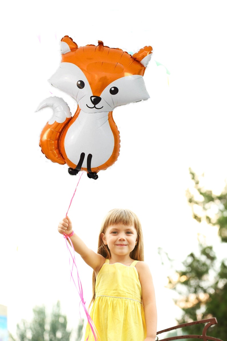 May include: A young girl in a yellow dress holds a large orange and white fox-shaped balloon with pink ribbon.