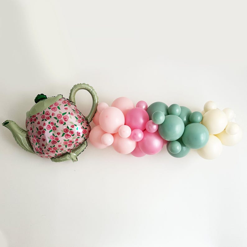 May include: A green and pink balloon garland with a green teapot balloon. The garland is made of pastel pink, light pink, and sage green balloons.