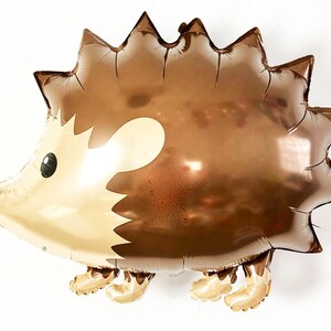 May include: A brown and gold foil balloon shaped like a hedgehog with a cute cartoon face. The balloon has a shiny metallic finish.