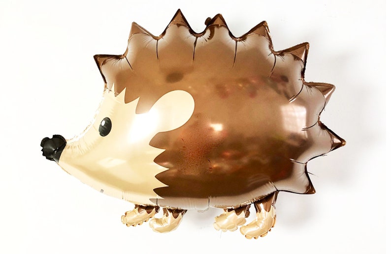 May include: A brown and gold foil balloon shaped like a hedgehog with a cute cartoon face. The balloon has a shiny metallic finish.