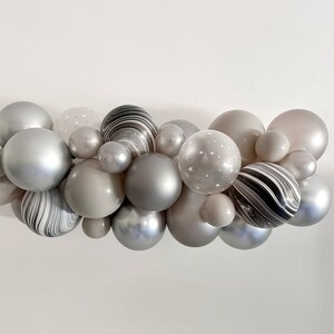 May include: A cluster of various sized balloons in shades of gray, silver, and white. Some balloons have a marbled effect, while others feature a star pattern. The arrangement is suitable for party decorations.