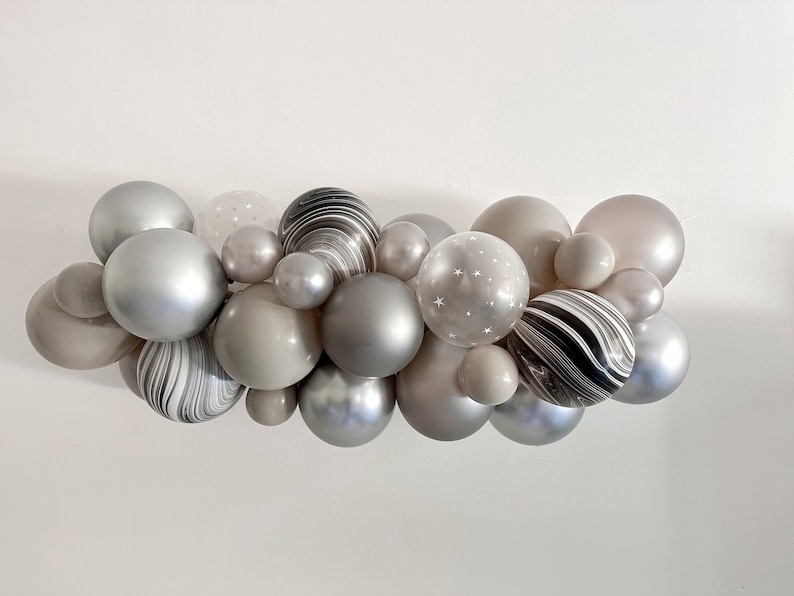 May include: A cluster of various sized balloons in shades of gray, silver, and white. Some balloons have a marbled effect, while others feature a star pattern. The arrangement is suitable for party decorations.
