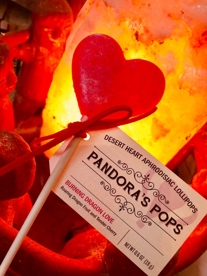 May include: A red heart-shaped lollipop on a stick with a white label that reads "DESERT HEART APHRODISIAC LOLLIPOPS PANDORA'S POPS BURNING DRAGON LOVE Roaring Dragon Fruit and Tender Cherry NET WT 0.6 OZ (18 g)"