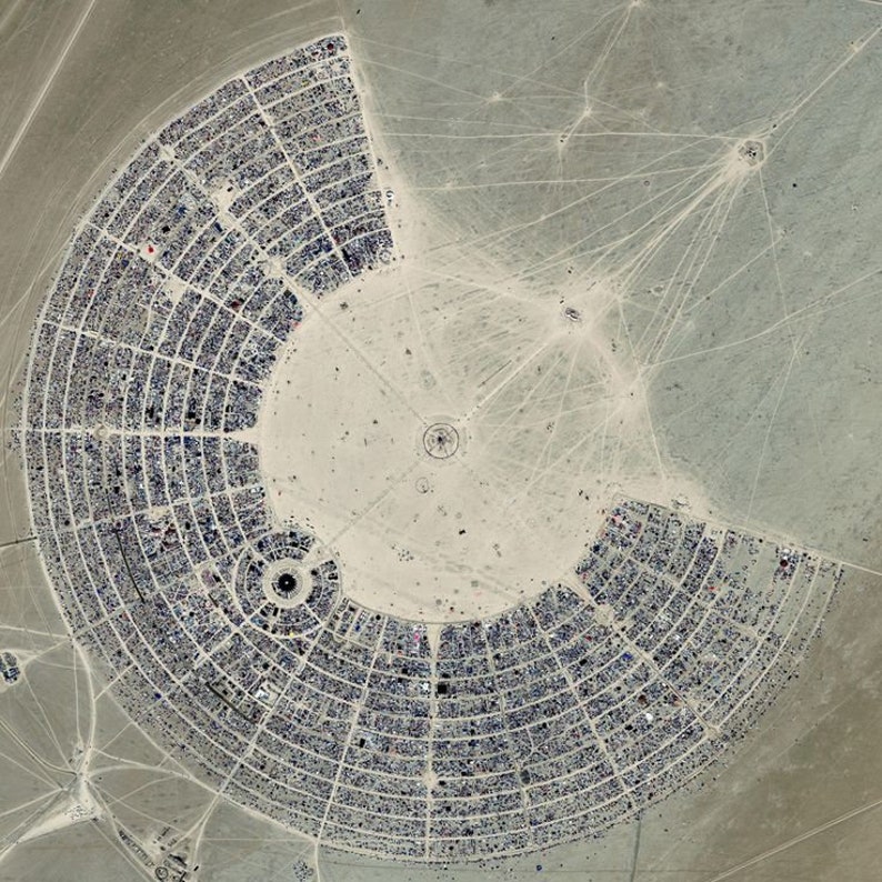 May include: An aerial view of a large, circular city built in the desert. The city is made up of a series of concentric circles, with a central plaza in the middle. The city is surrounded by a vast, empty desert.