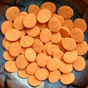 May include: A bowl filled with small, oval-shaped, orange-colored candies. The candies have a textured surface and a subtle design.