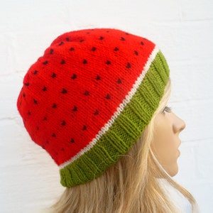 Puede incluir: Sombrero de punto rojo y verde con diseño de sandía. El sombrero tiene una franja blanca entre las secciones roja y verde.
