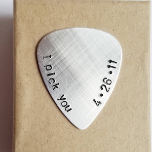 Könnte beinhalten: Ein silberner Gitarrenplektrum mit dem Text "I pick you" und dem Datum "4.26.11" eingraviert.