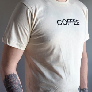 Light coloured, short sleeve t-shirt screen printed to say Coffee in dark font.