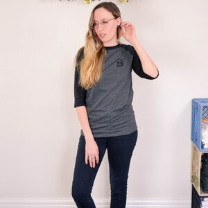 Raglan half length sleeve t-shirt in dark colours, screen printed to say Team No Fun in small type, modelled in dark pants and shoes to show full length of shirt.