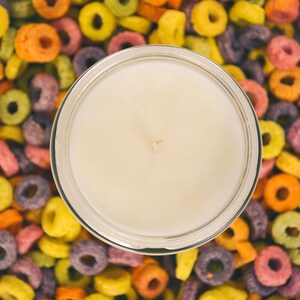 Large container candle in clear glass jar with metal lid, shown with colourful Froot Loops cereal as background.