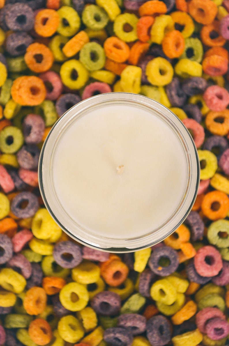 Large container candle in clear glass jar with metal lid, shown with colourful Froot Loops cereal as background.