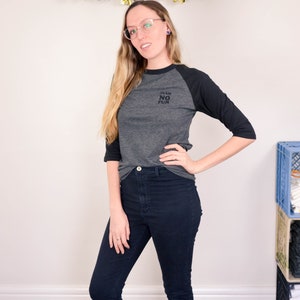 Raglan half length sleeve t-shirt in dark colours, screen printed to say Team No Fun in small type, modelled in dark pants and shoes to show it tucked in.