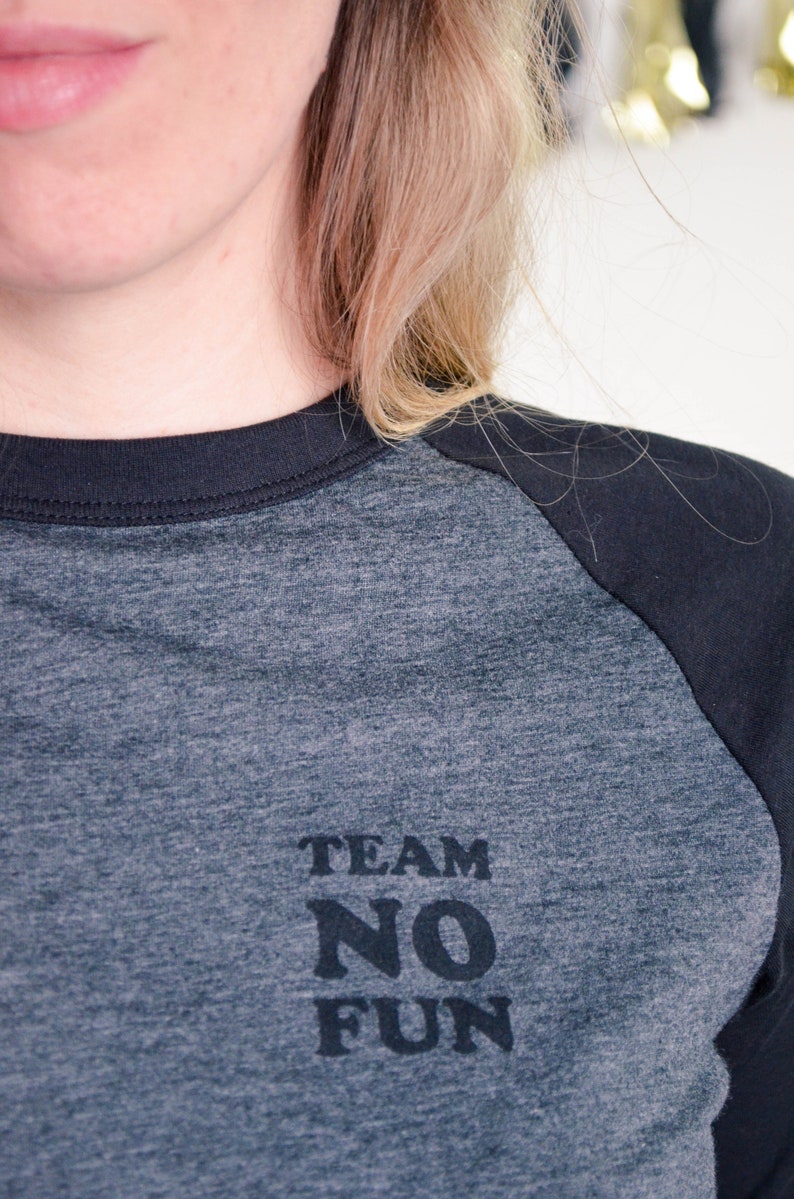 Close up of t-shirt in dark colours, screen printed to say Team No Fun in small, dark coloured type.