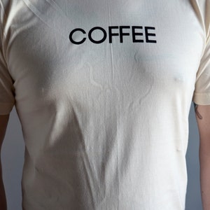 Light coloured, short sleeve t-shirt screen printed to say Coffee in dark font.