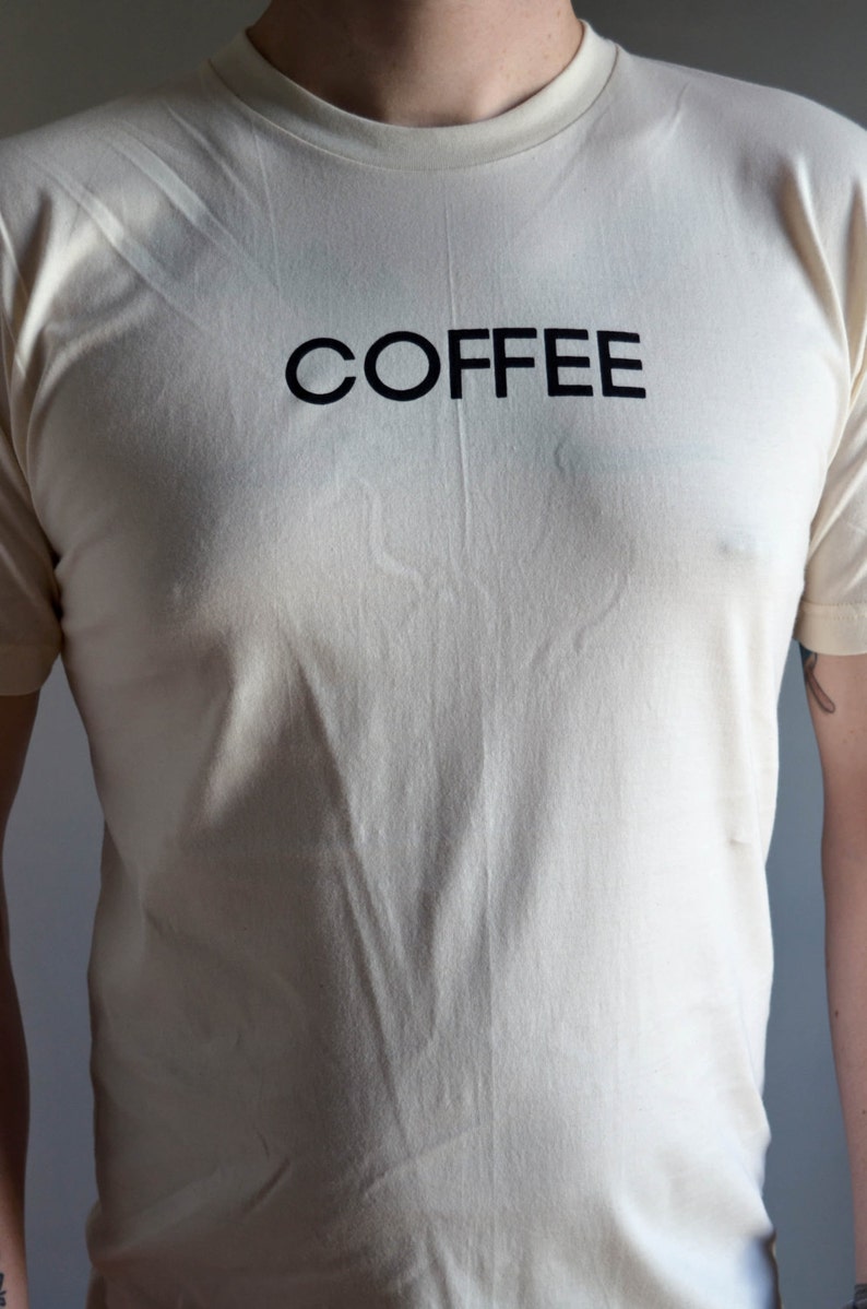 Light coloured, short sleeve t-shirt screen printed to say Coffee in dark font.