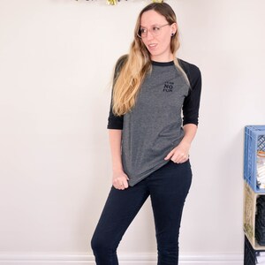 Raglan half length sleeve t-shirt in dark colours, screen printed to say Team No Fun in small type, modelled with dark pants and shoes.